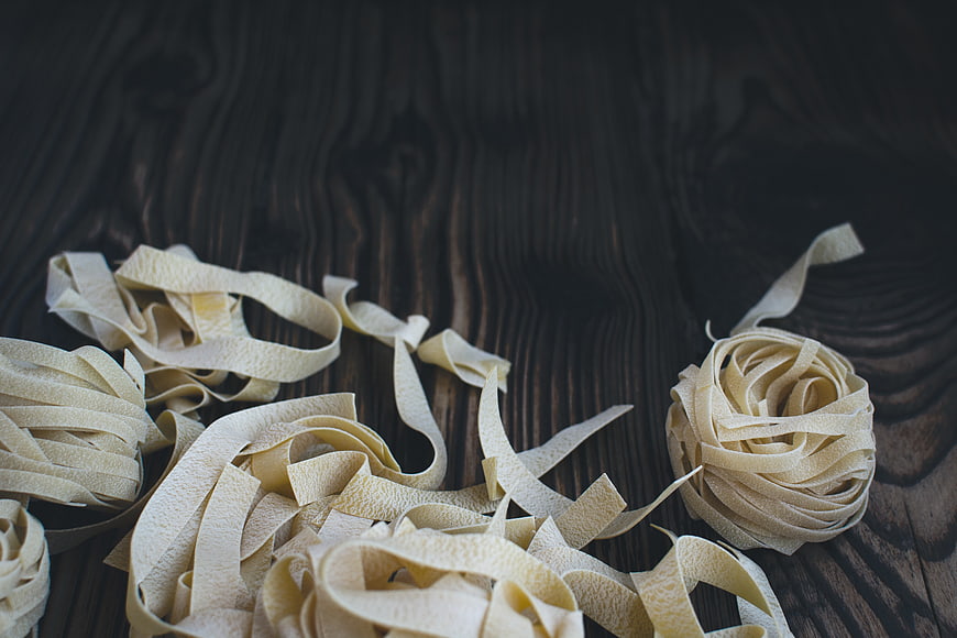 Fresh handmade tagliatelle pasta nests on dark rustic wood