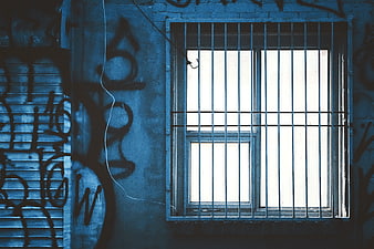 Blue tinted window with bars and graffiti on urban wall