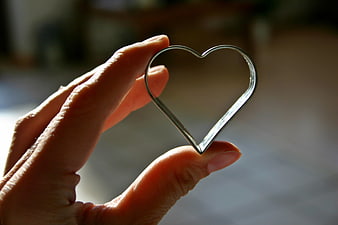 Hand holding a silver heart-shaped cookie cutter against a blurred background