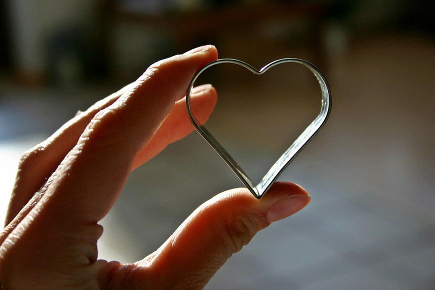 Hand holding a silver heart-shaped cookie cutter against a blurred background