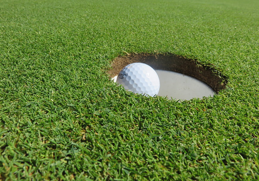 Golf ball resting on the edge of a putting green hole