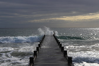 Wooden pier extending into stormy ocean with crashing waves