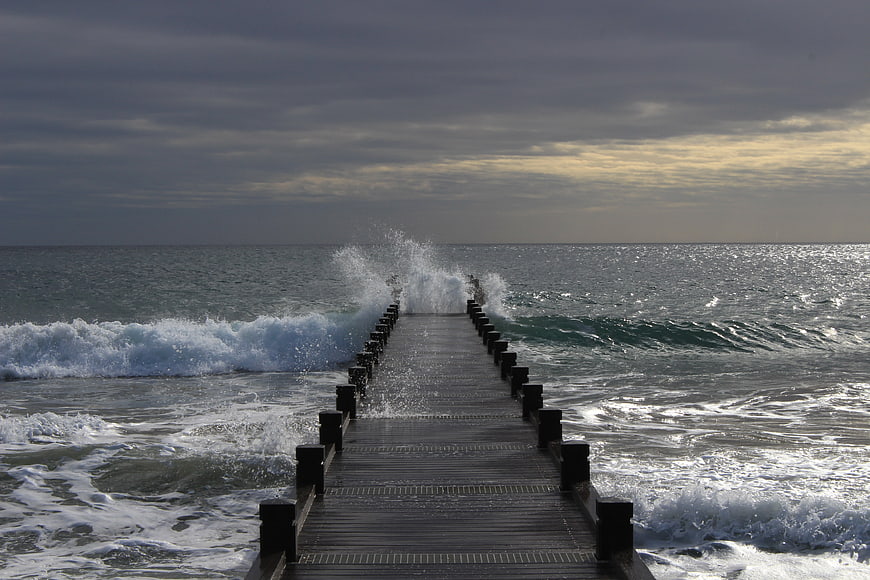Wooden pier extending into stormy ocean with crashing waves