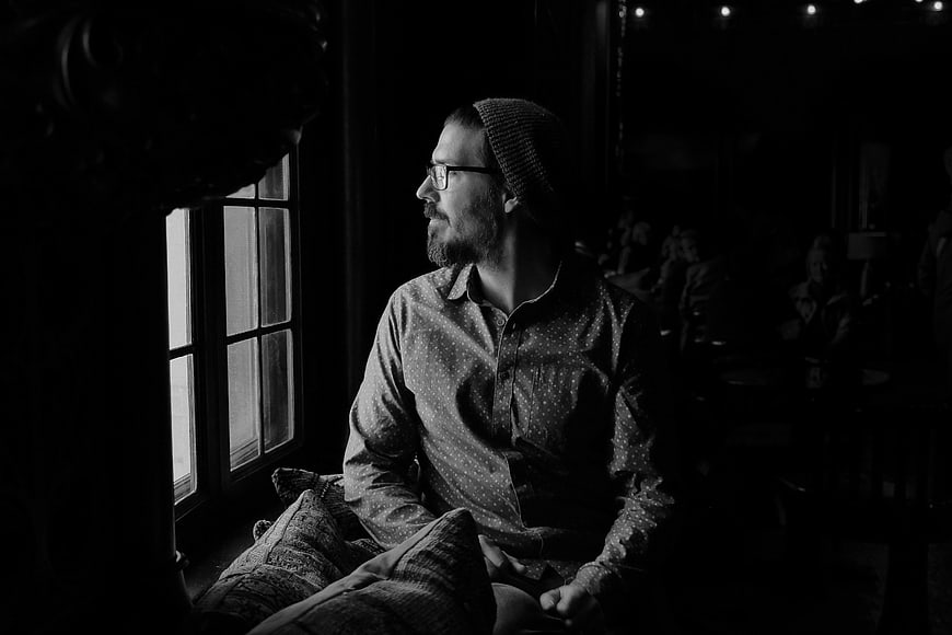Contemplative Man in Beanie Looking Out Window in Black and White