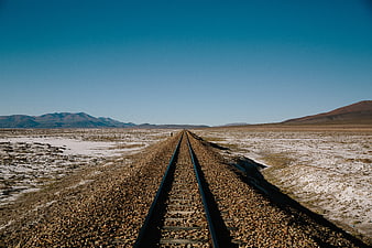 Desert railway tracks leading to distant mountains under a clear blue sky