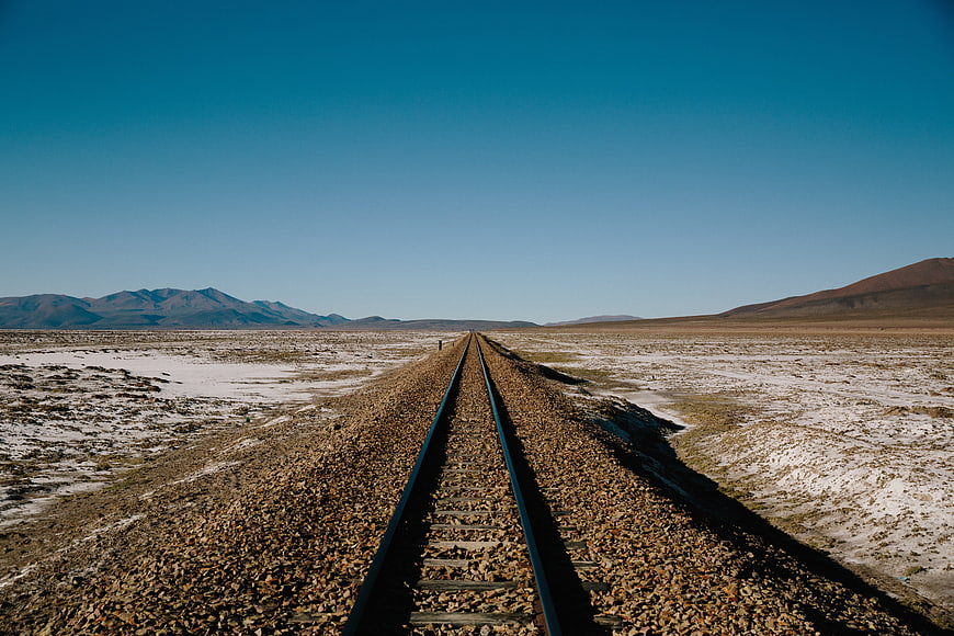 Desert railway tracks leading to distant mountains under a clear blue sky