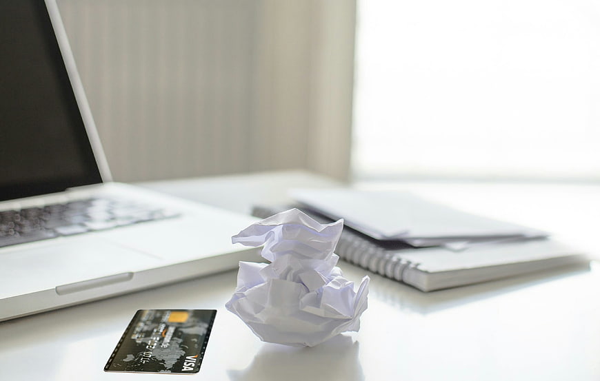 Crumpled paper and credit card on white desk with laptop