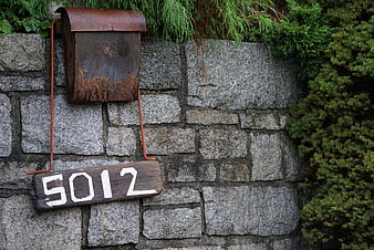 Rusty vintage mailbox and house number on stone wall