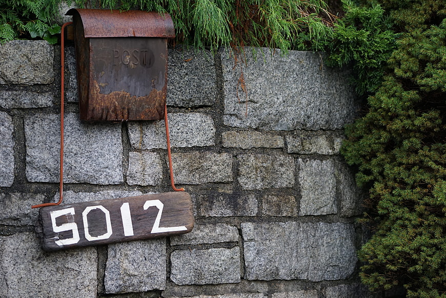 Rusty vintage mailbox and house number on stone wall