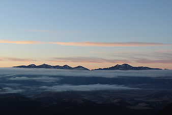 Snow-capped mountain peaks rising above a sea of clouds at sunrise