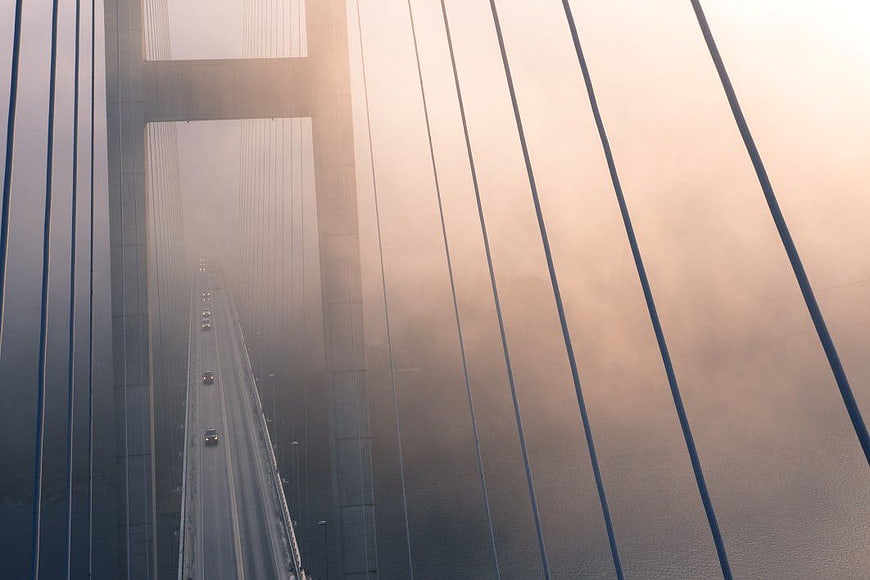 Foggy Suspension Bridge with Cars Driving at Dawn