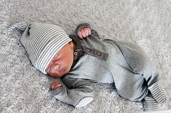 Sleeping newborn baby in grey outfit on fluffy rug