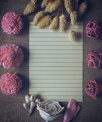 Flat lay of lined paper with pink flowers and dried grass on burlap