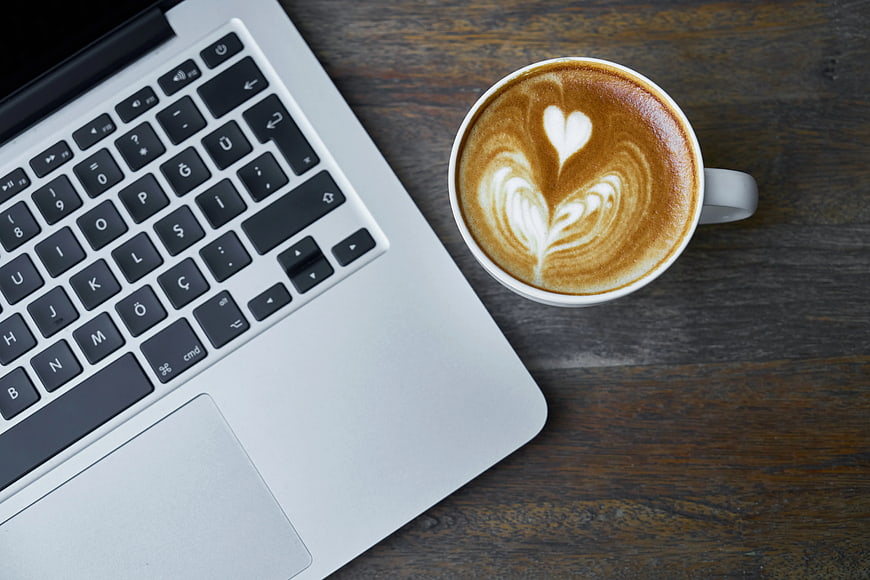 Flat lay of laptop and latte art coffee on wooden desk