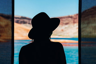 Silhouette of woman in hat looking out at ocean