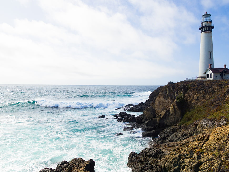 White Lighthouse on Rocky Coastal Cliff Overlooking Ocean Waves