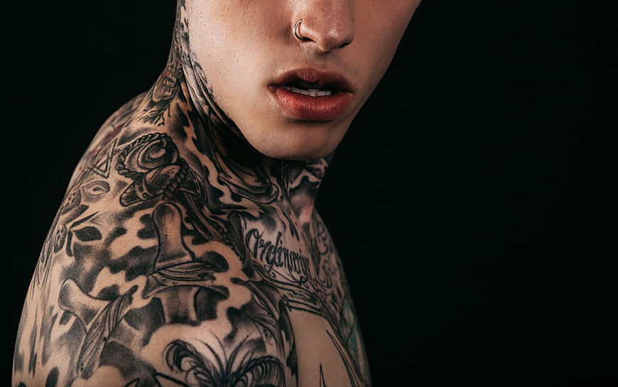 Close-up of man with neck and shoulder tattoos on black background