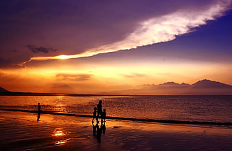 Silhouette of family walking on beach at sunset with mountains