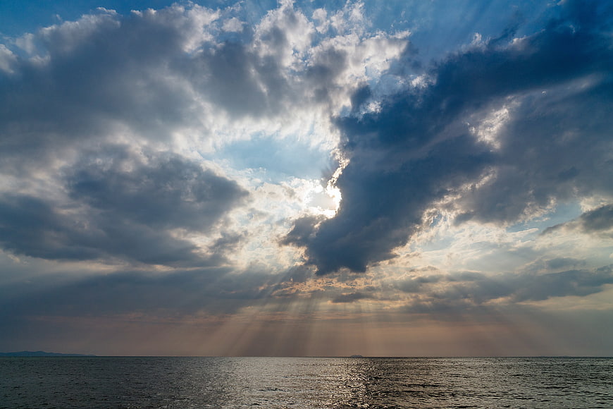 Dramatic Sunbeams Breaking Through Clouds Over Ocean Horizon