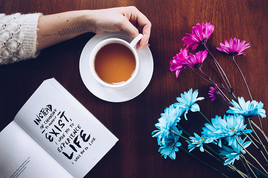 Flat lay of tea cup, open book with quote, and colorful flowers