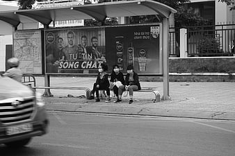 Three young women wearing face masks sitting at a bus stop in Vietnam