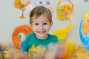 Smiling young boy in green shirt holding pen in colorful classroom