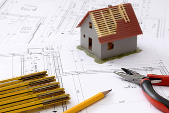 Architectural house model with blueprints, pencil, and pliers on desk