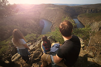 Friends sitting on cliff edge overlooking winding river canyon