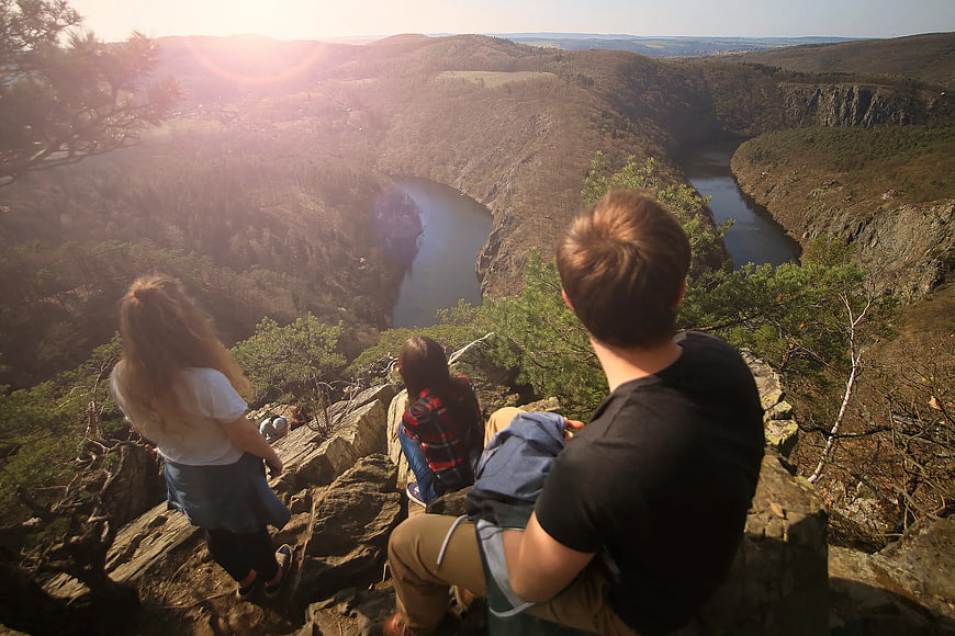 Friends sitting on cliff edge overlooking winding river canyon