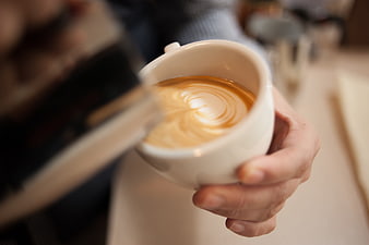 Close-up of hand holding white cup with latte art in cozy cafe