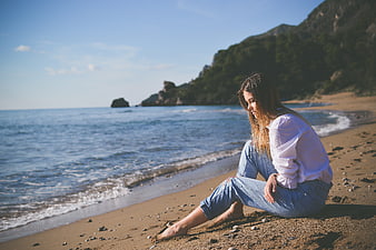 Woman sitting alone on sandy beach looking at ocean
