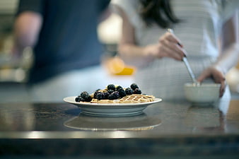 Waffles with blackberries on kitchen counter with blurred couple