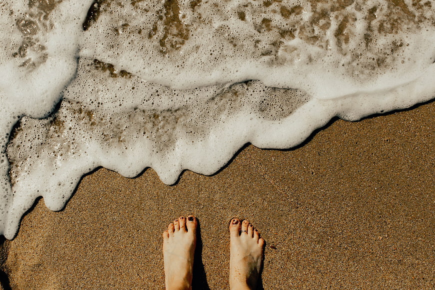Top View of Bare Feet on Sandy Beach with Ocean Foam
