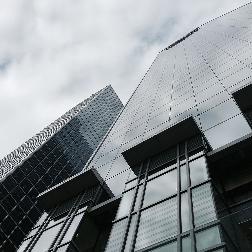 Low angle view of modern glass skyscrapers against cloudy sky
