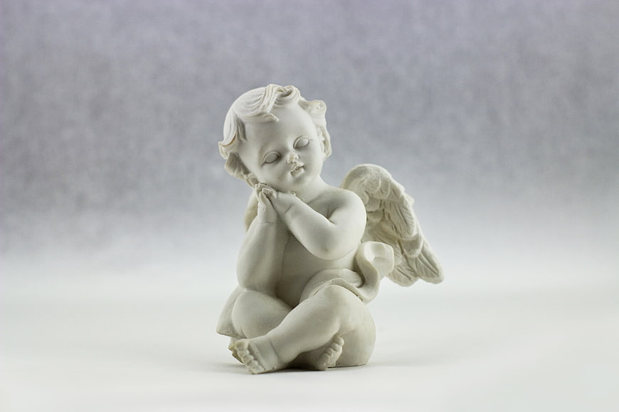 White porcelain praying angel figurine on gray background