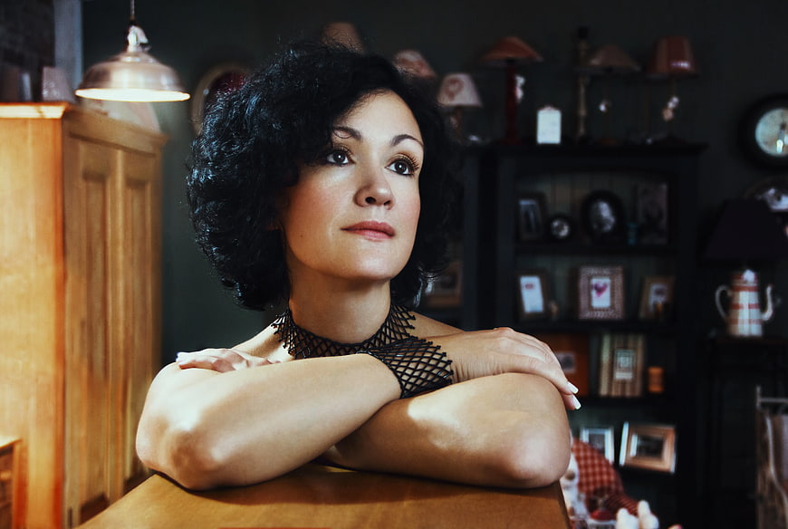 Woman with curly hair leaning on wooden table in vintage room