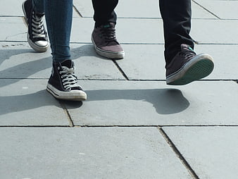 Close-up of two people walking on pavement in sneakers