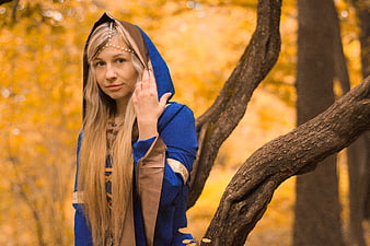 Woman in blue medieval costume standing in autumn forest