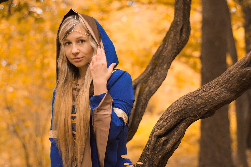 Woman in blue medieval costume standing in autumn forest
