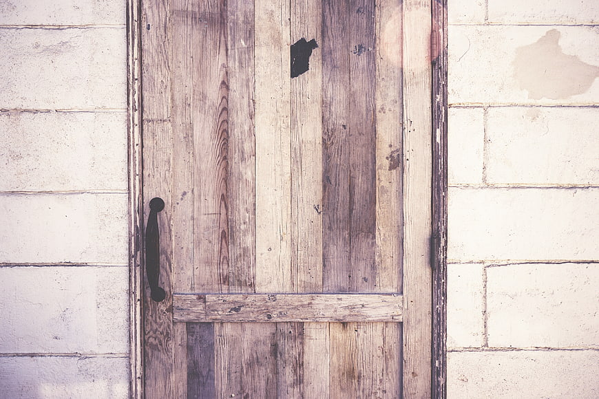 Rustic wooden door with black handle on white brick wall