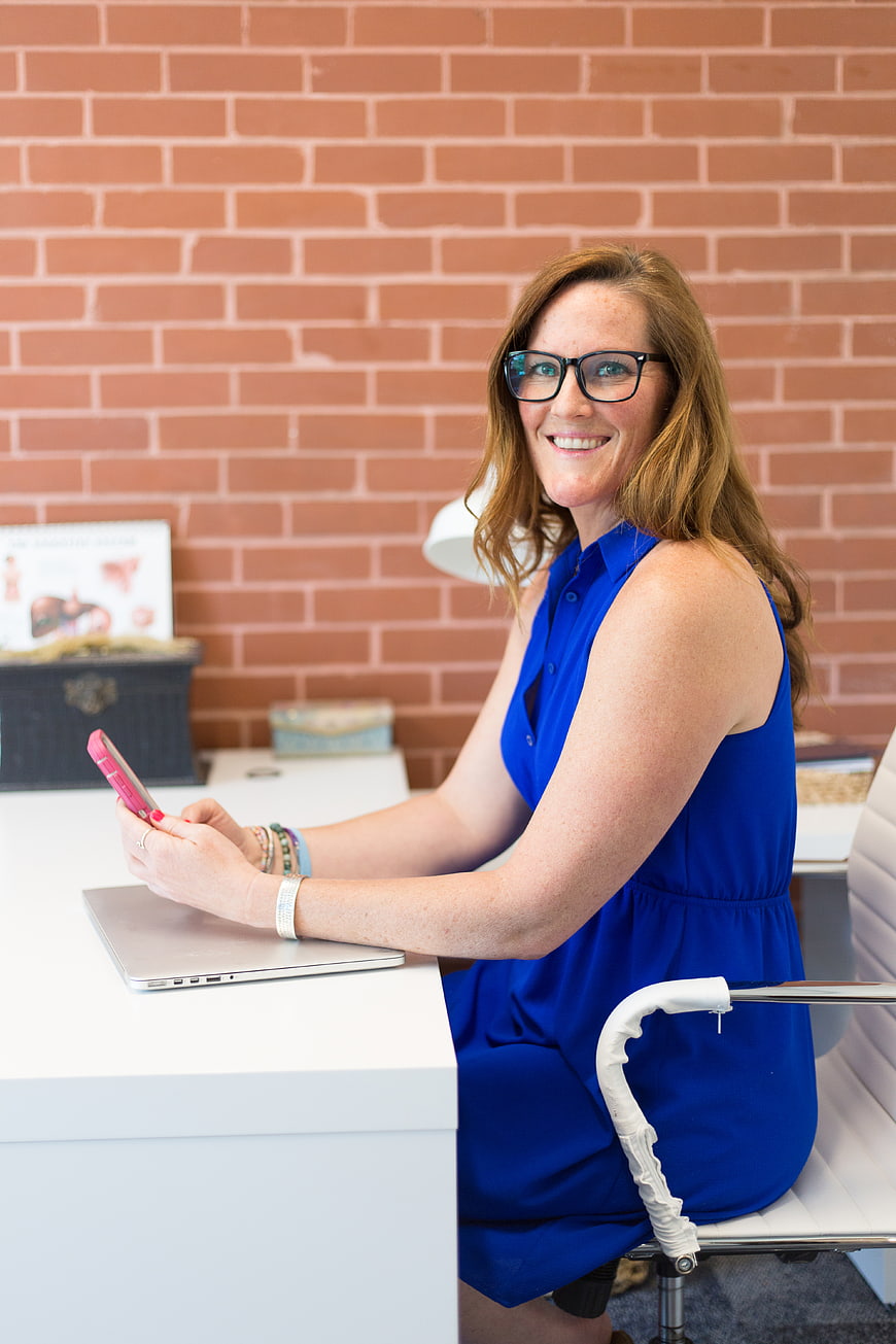 Smiling Business Woman with Smartphone at Office Desk