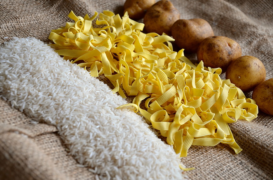 Raw pasta, rice, and potatoes on burlap background
