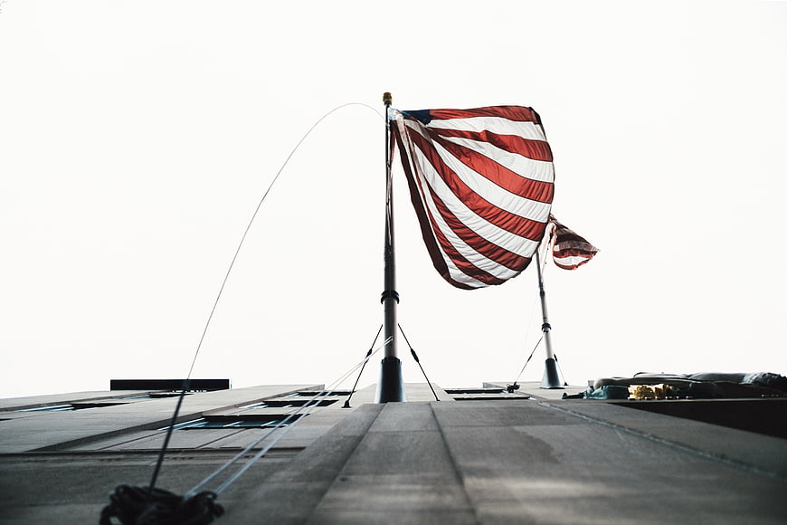 American Flag Waving on Rooftop Against White Sky