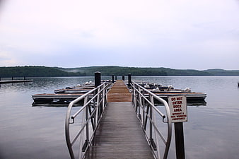 Wooden dock leading to lake with boats and forest hills