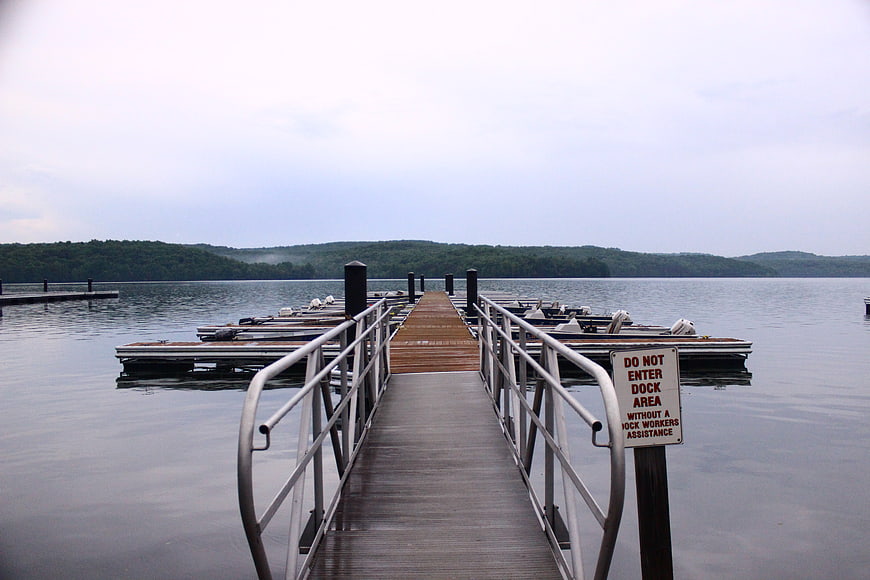 Wooden dock leading to lake with boats and forest hills