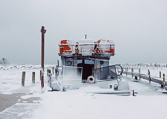 Snow-covered pontoon boat docked at frozen winter pier