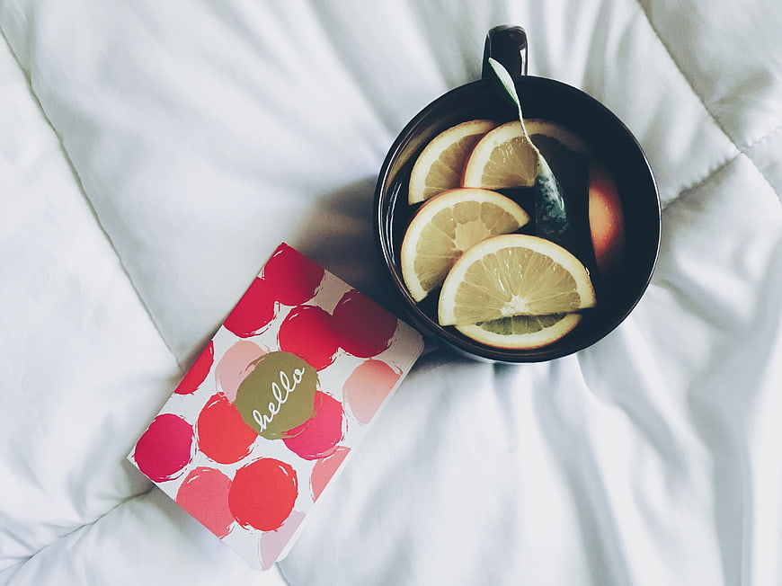 Flat lay of hot tea with lemon slices and greeting card on white bed