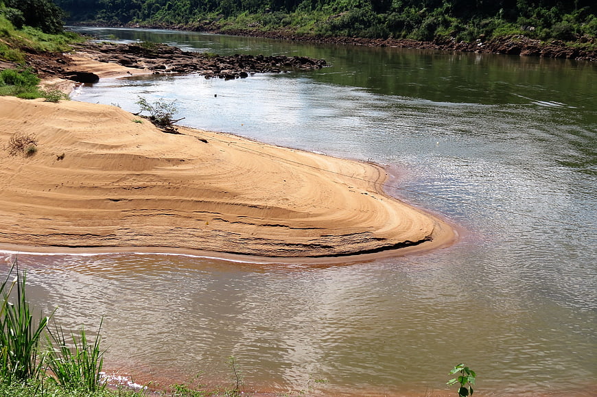 Sandy riverbank with flowing water and lush green forest background