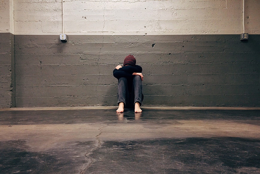 Lonely person sitting barefoot against concrete wall