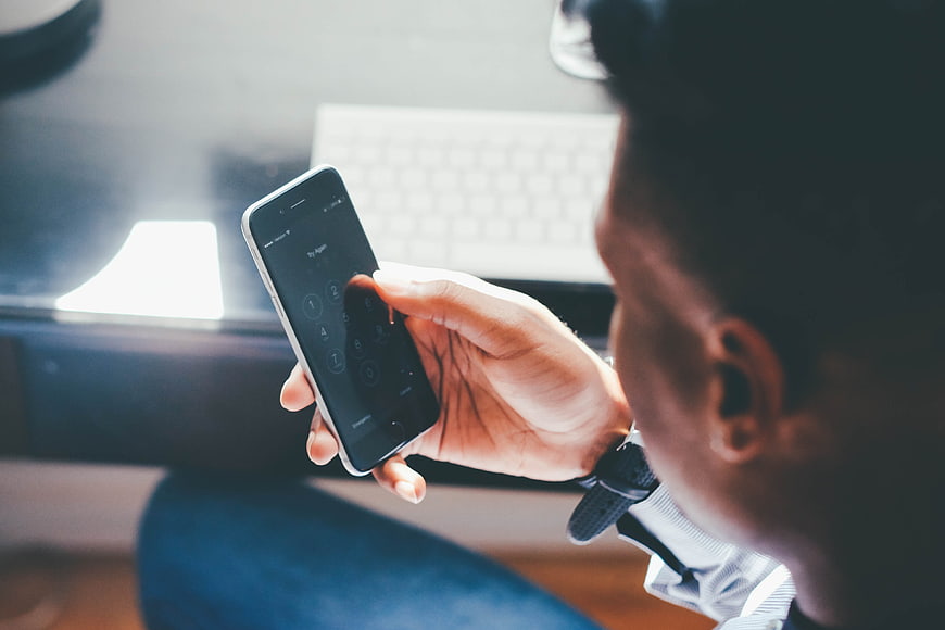 Man Entering PIN Code On Smartphone Screen In Office